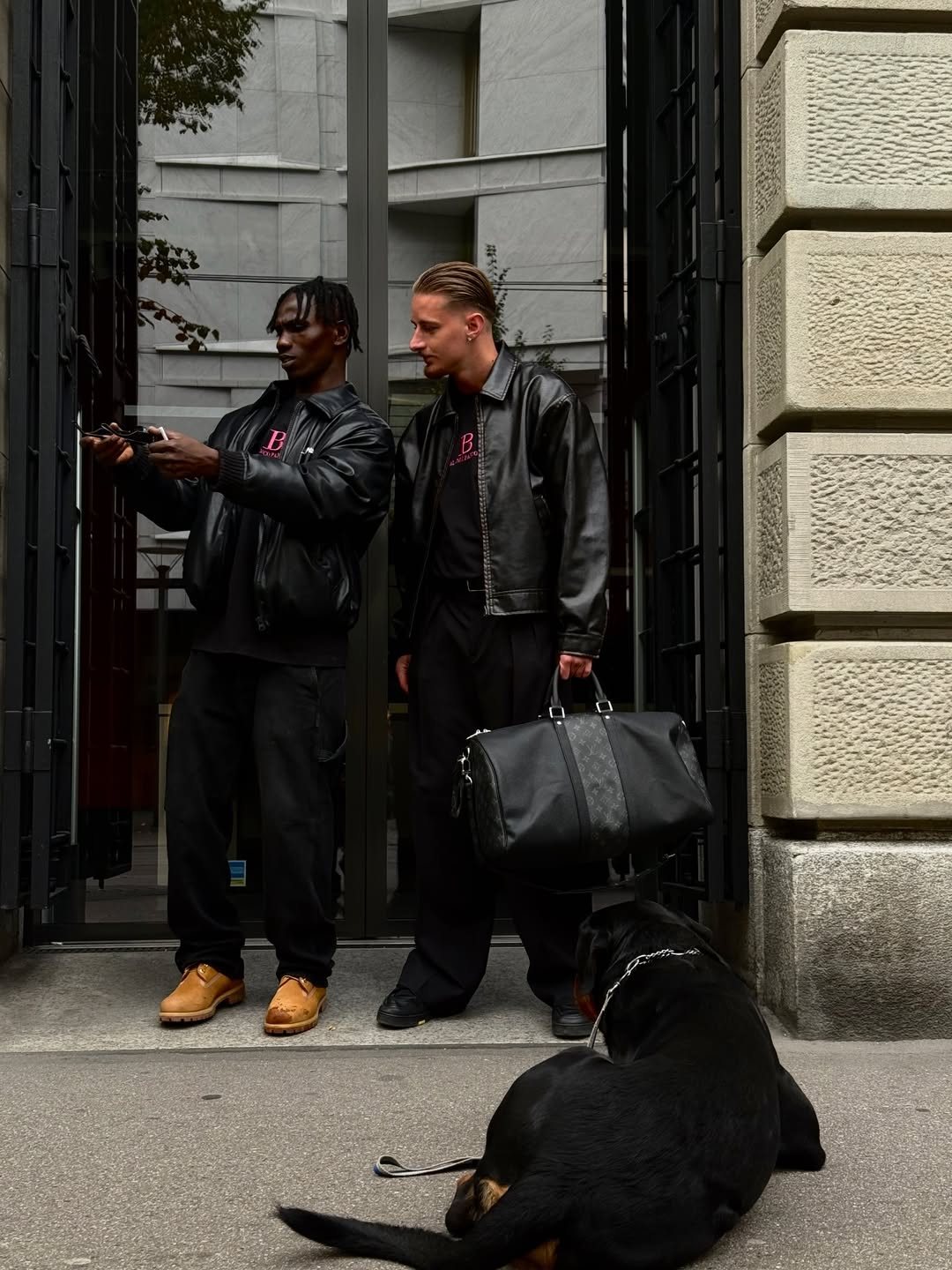 Two men in black BLANCO PARDON outfits with a Rottweiler at a doorway