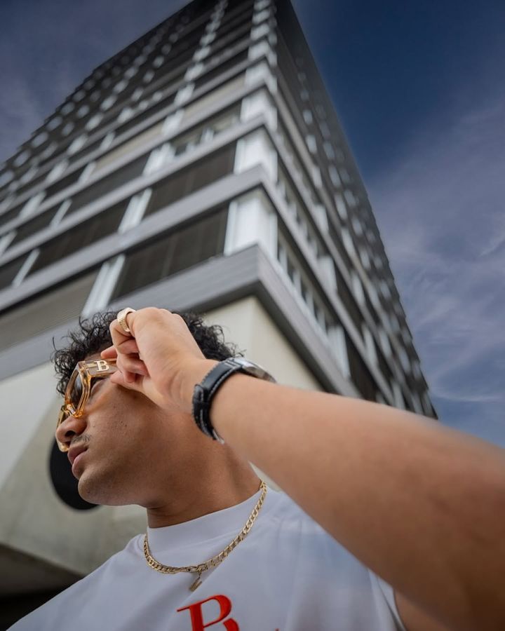 Man in a white BLANCO PARDON T-shirt in front of a high-rise